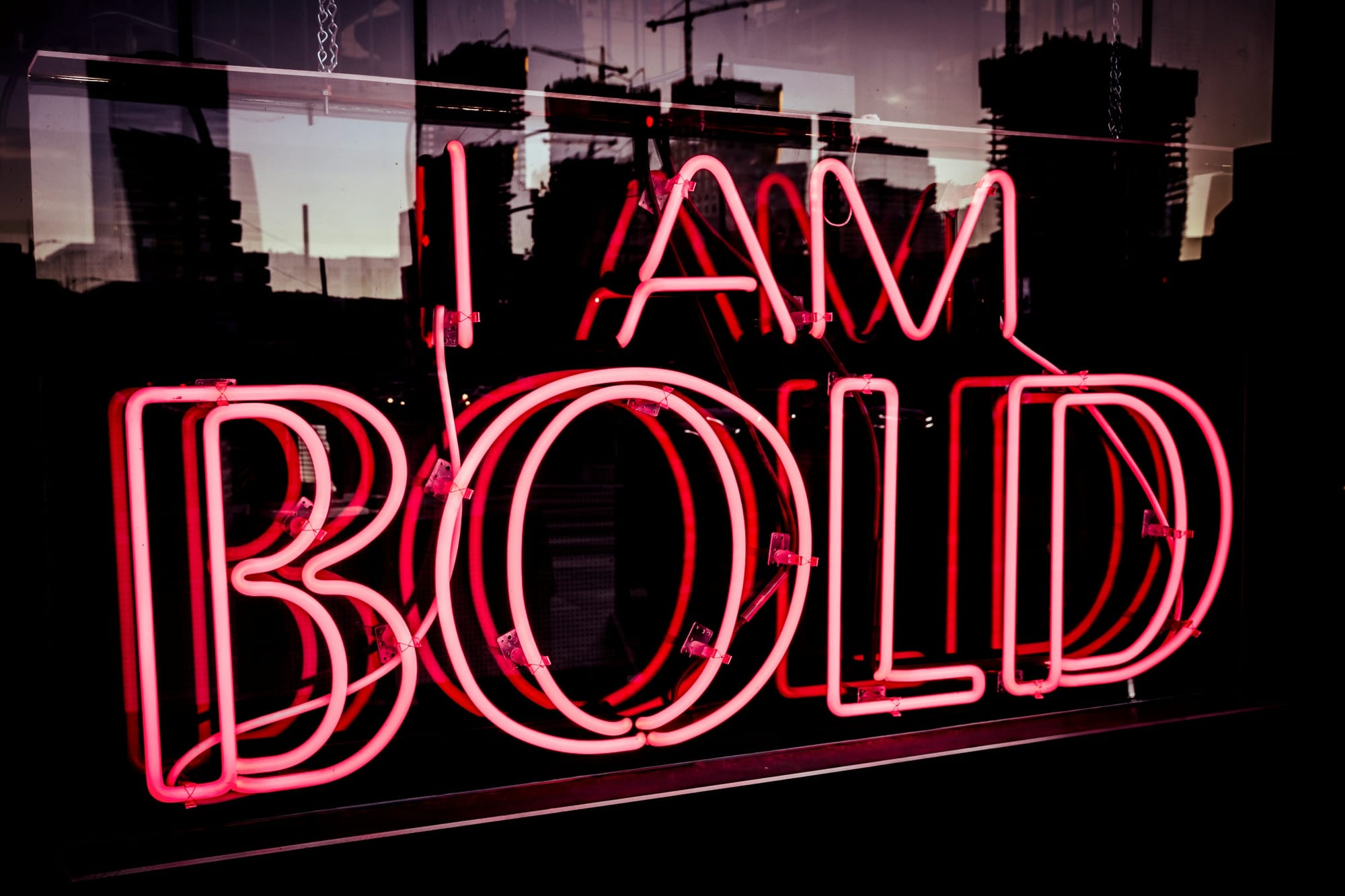  En lysande röd neonskylt med texten "I am bold" i klassisk 90-talsstil. Neonljuset ger en stark och självsäker känsla, med en djärv och modern design inspirerad av retroestetik. Skylten lyser upp sin omgivning och skapar en nostalgisk men samtidigt trendig atmosfär, perfekt för en 90-tals temafest eller en urban inredning.