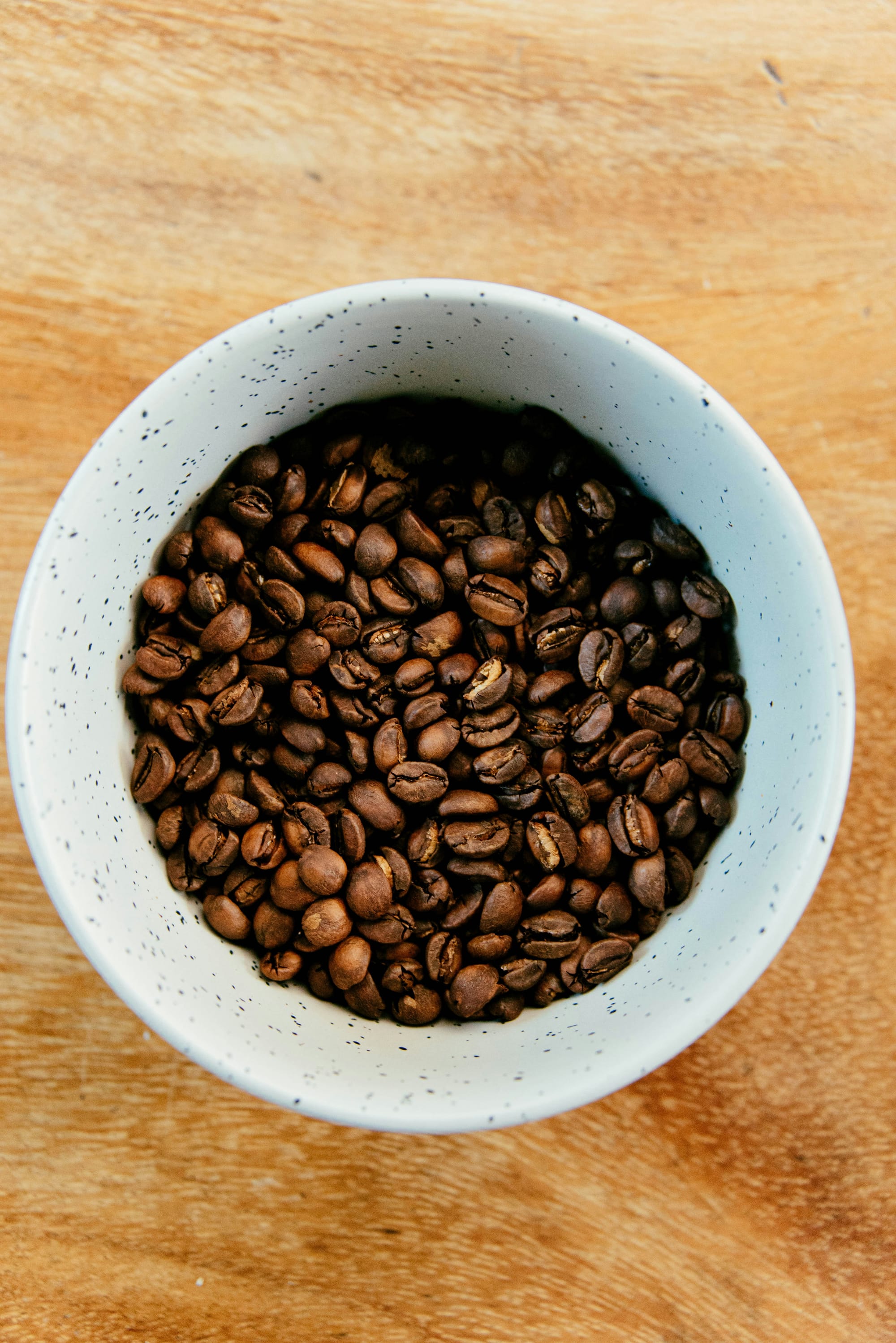 En vit skål fylld med hela kaffebönor på ett träbord.