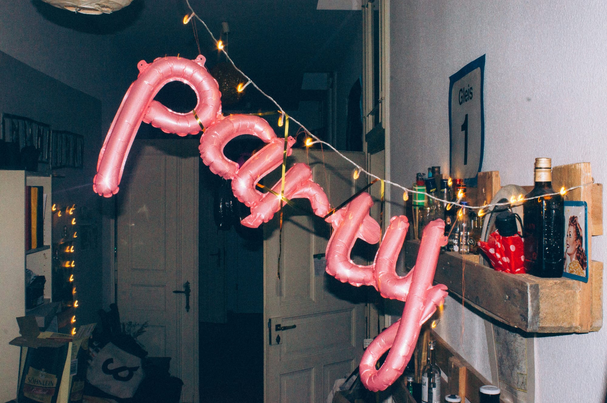 Rosa folieballonger som stavar ordet "party", upphängda med ljusslinga i en festdekorerad hall.