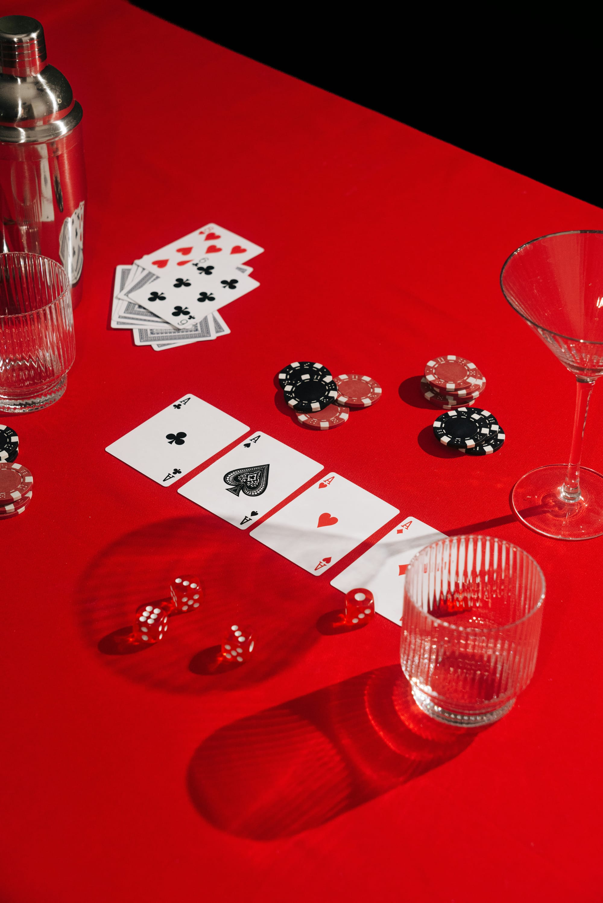 En röd duk med pokerkort utlagda och tärningar bredvid marker och cocktailglas. Bordet är dukat för en fest med stillasittande vuxenlekar och potentiella dricklekar.