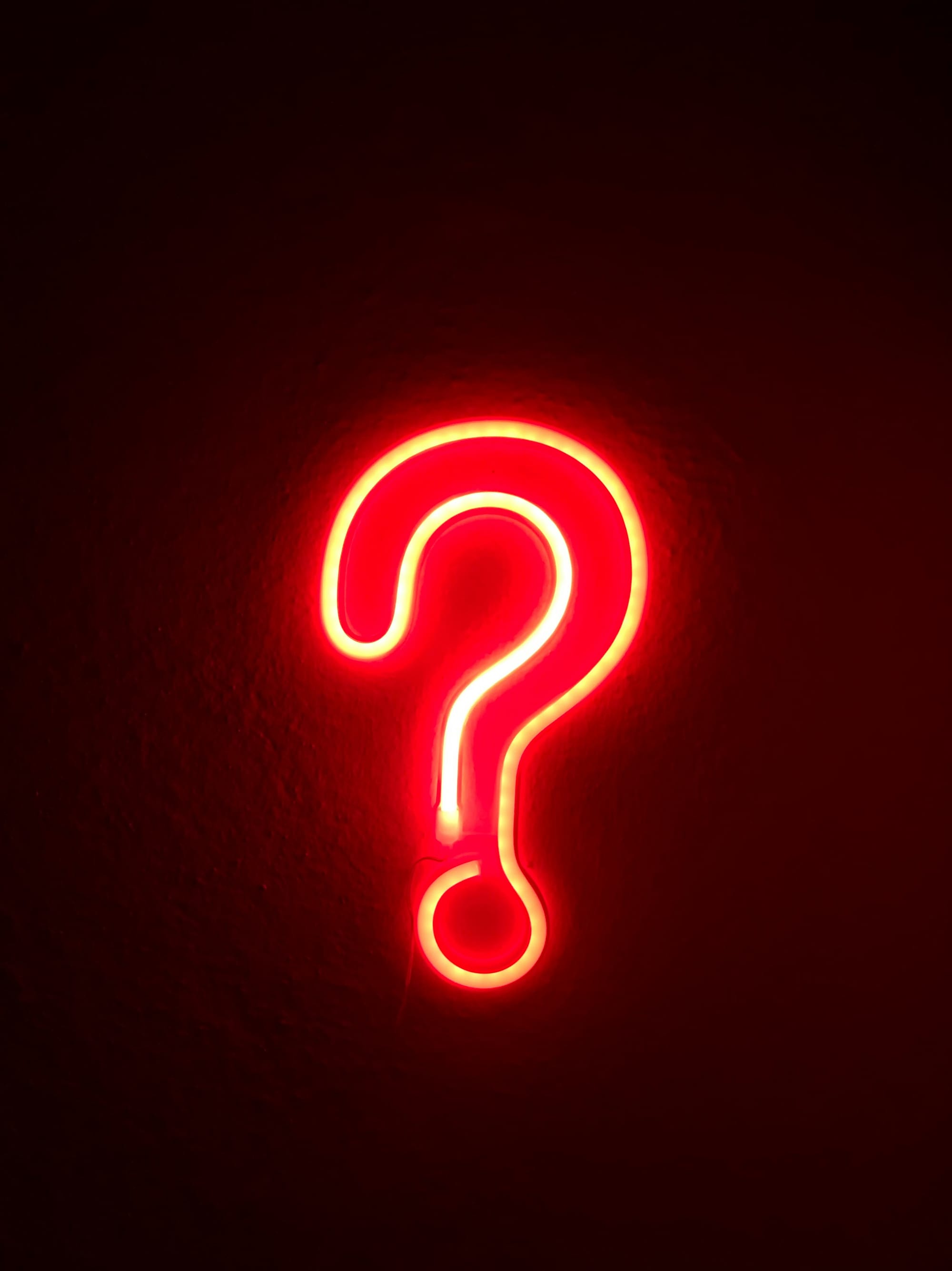 Lysande rött neonfrågetecken mot mörk bakgrund, symboliserar kluriga quiz frågor och gåtor för vuxna på fest.