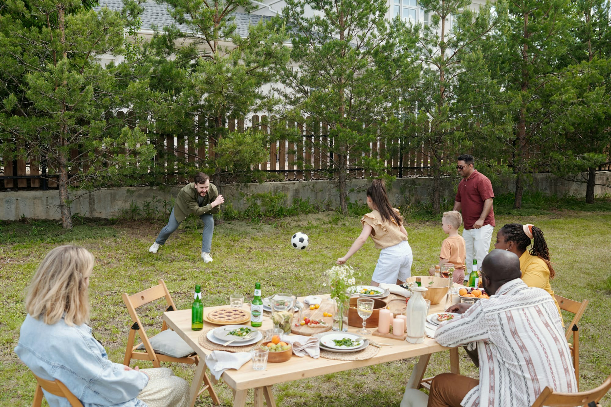 Utomhuslekar på valborgsfest – familj spelar boll och umgås vid ett somrigt dukat festbord i trädgården.