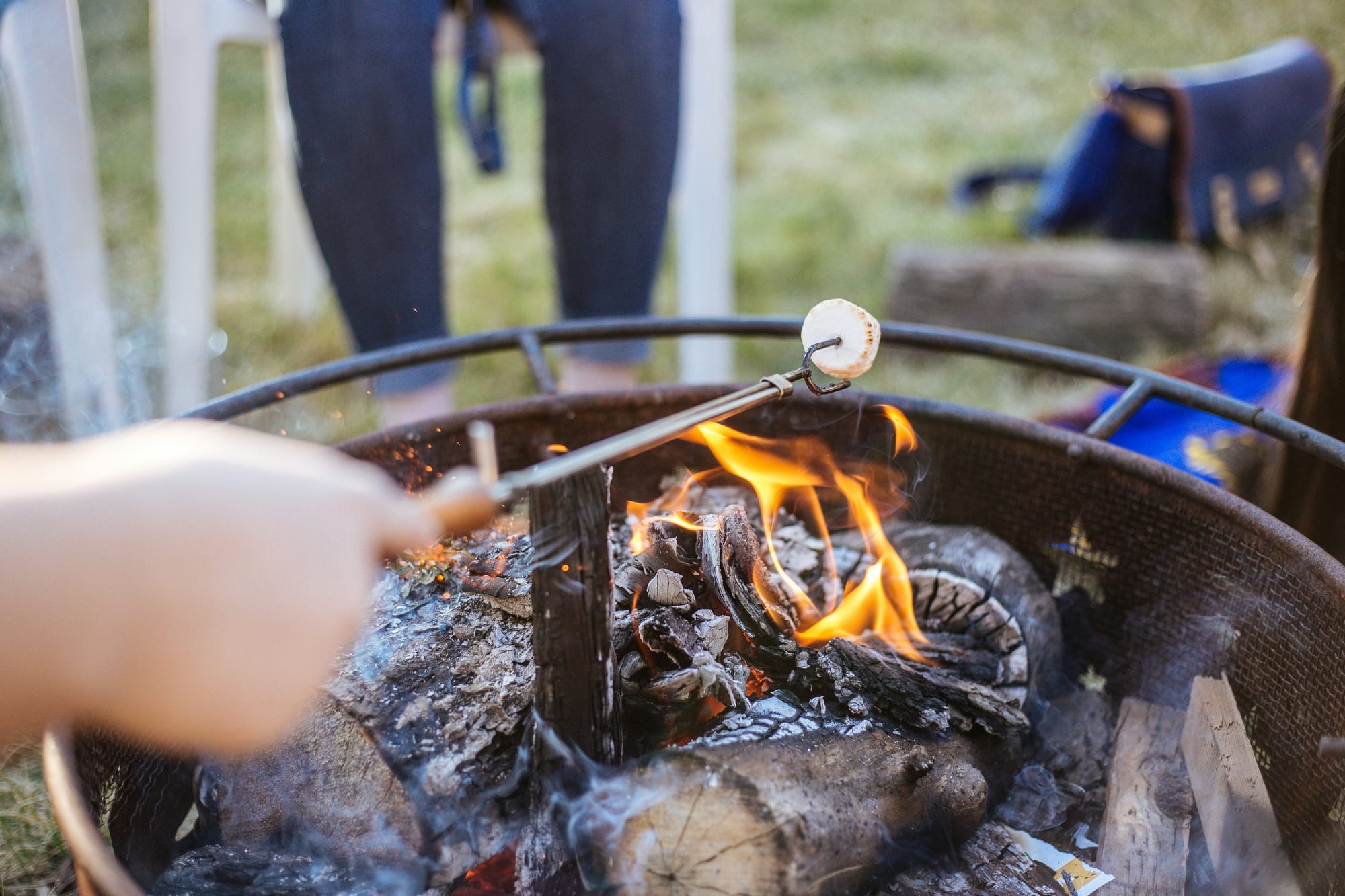 Person grillar marshmallows vid öppen eld under en valborgsfest med lekar, värme och gemenskap i trädgården.